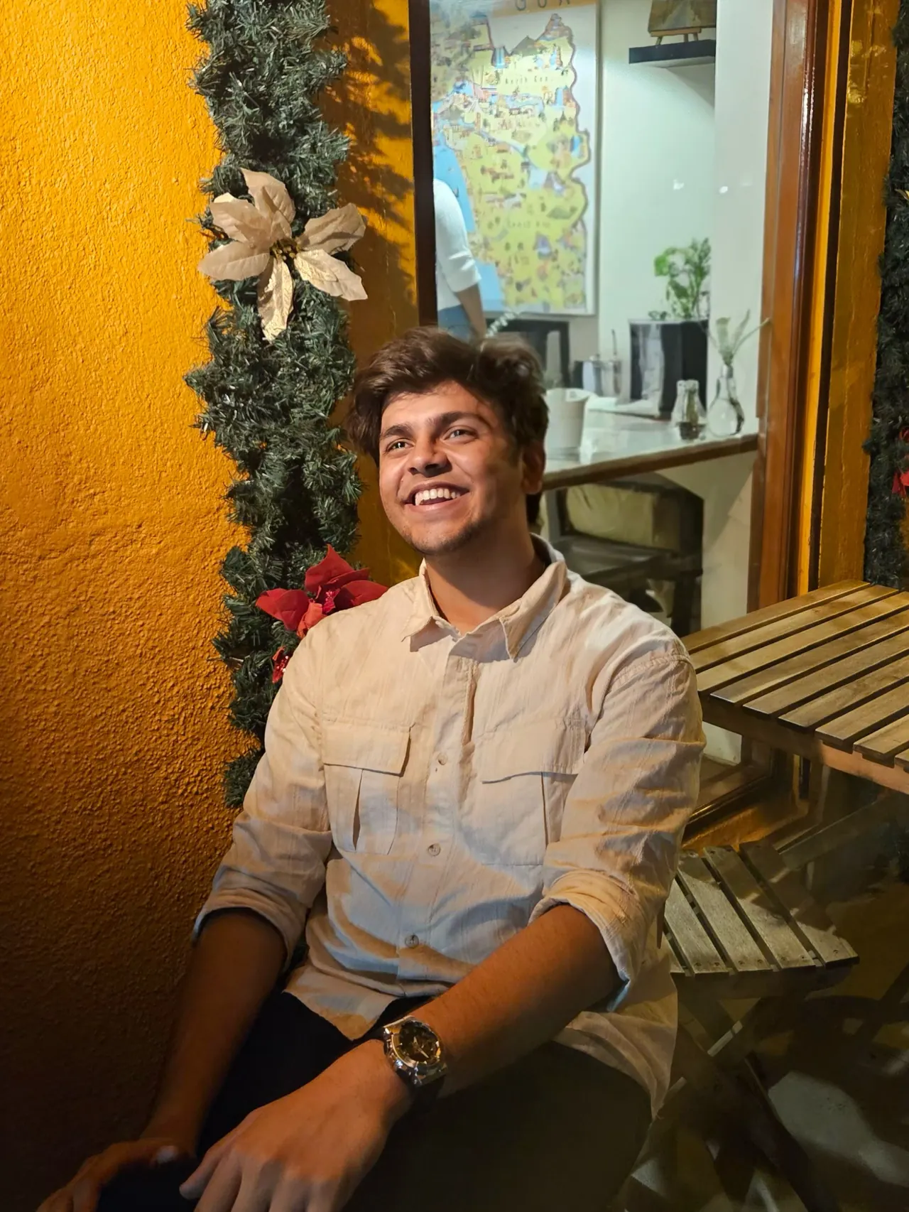 Aditya sitting in a warmly lit cafe, smiling and looking away